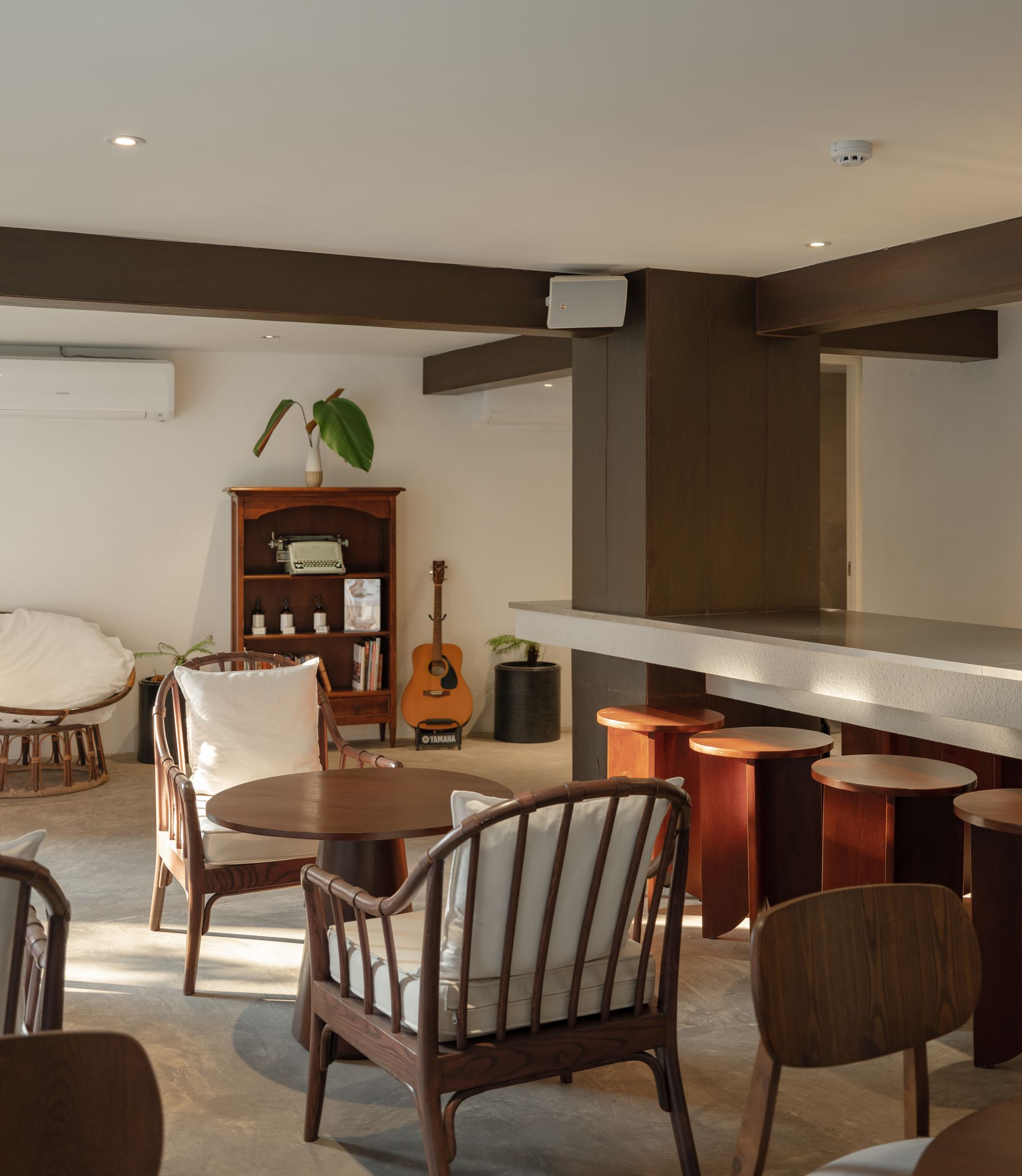 Modern lounge with wooden tables, striped chairs, bar stools, and a small cabinet in a warmly lit room