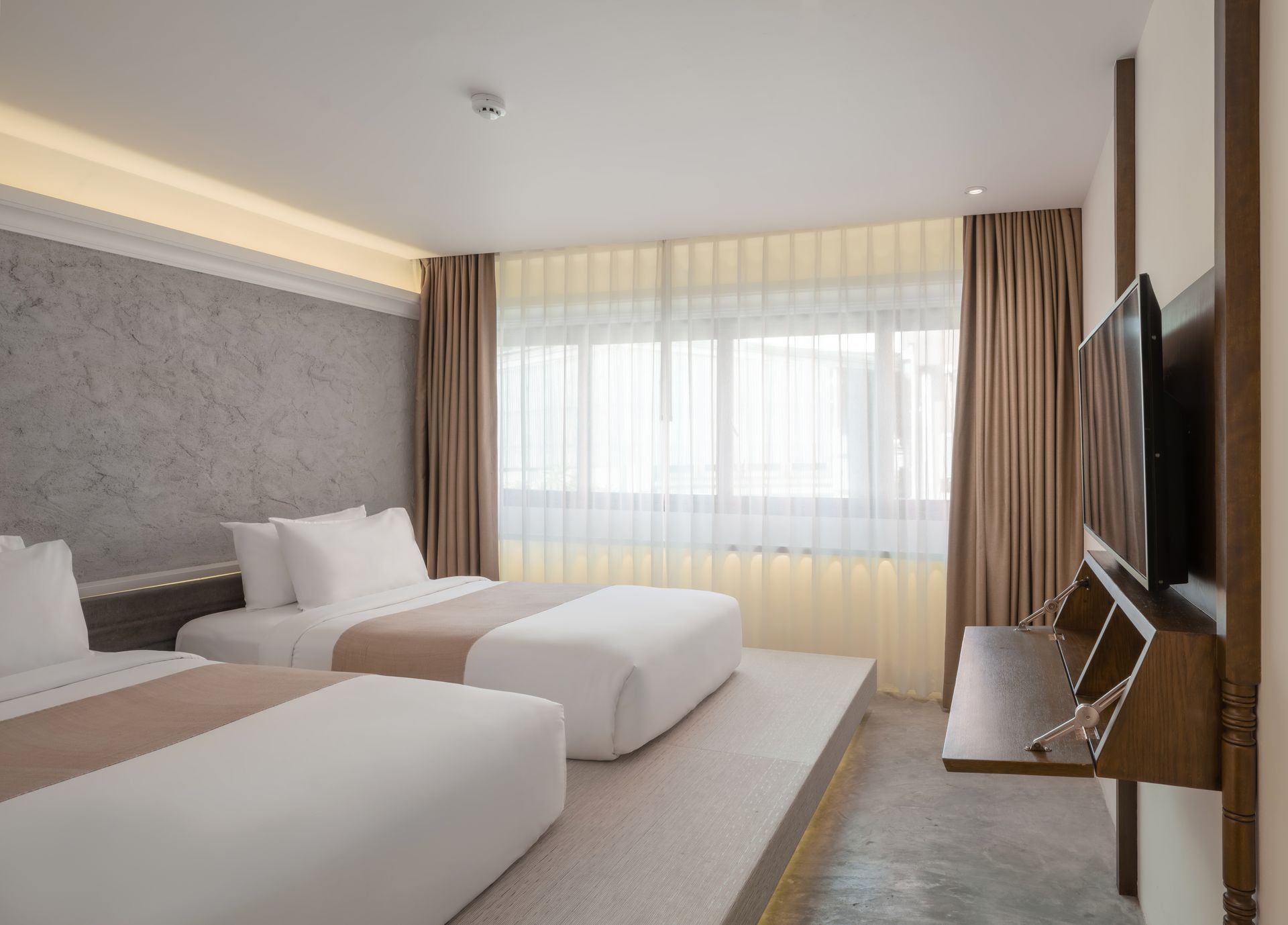 Modern hotel room with two twin beds, large window, and wall-mounted TV