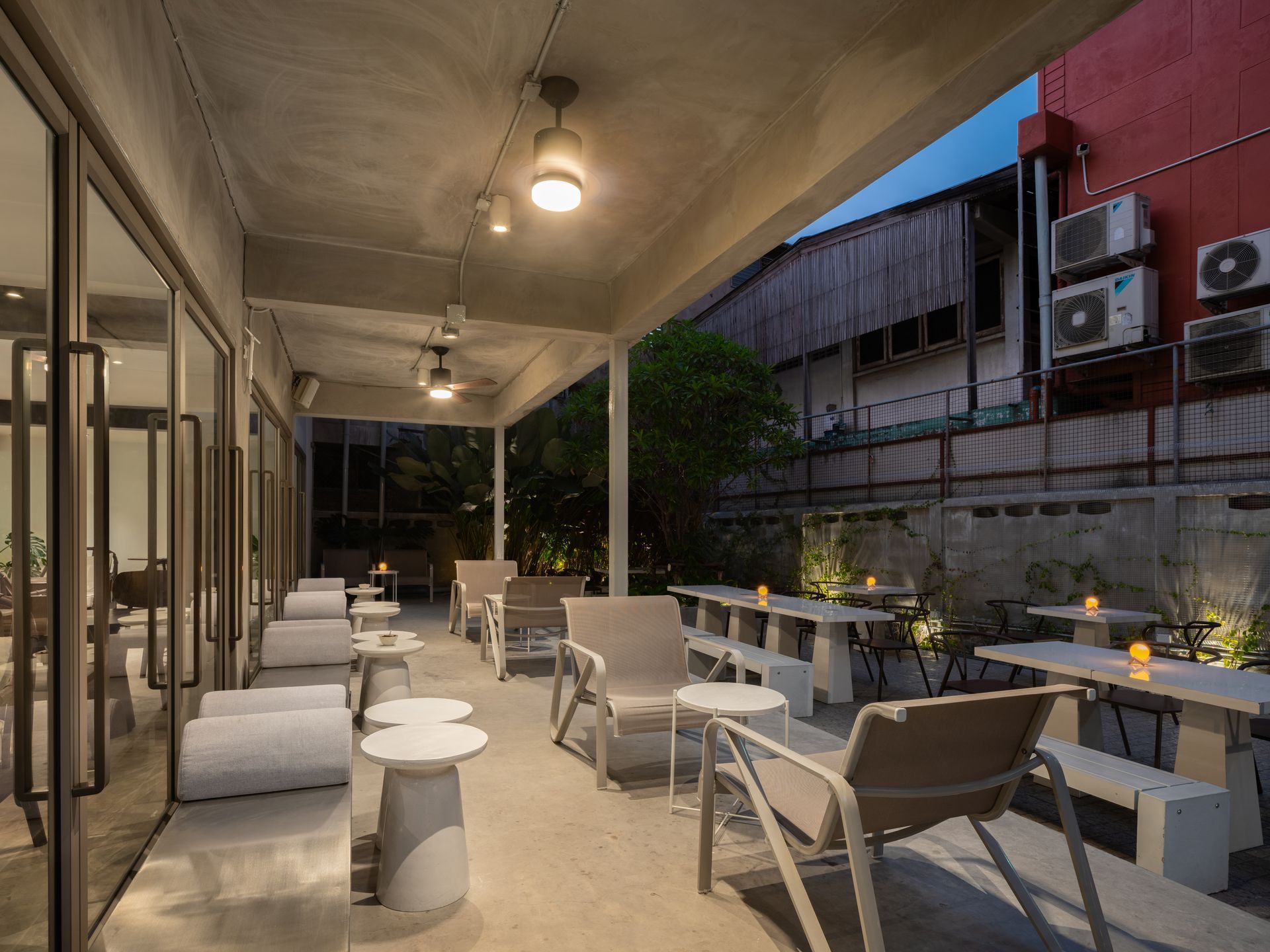 Covered outdoor patio with white tables and chairs, warm lights, and brick walls at dusk