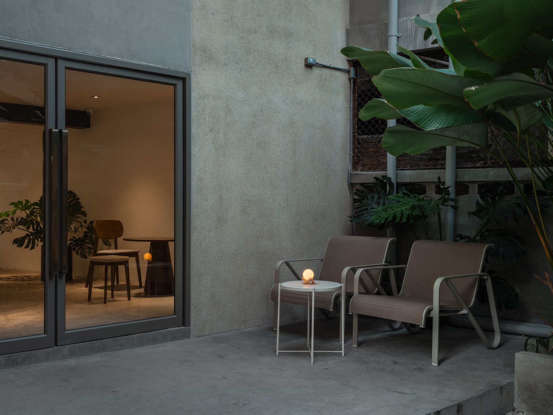 Modern patio with two lounge chairs, side table, lit candle, and sliding glass doors to a warm interior