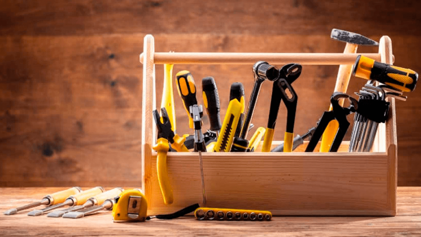 Wooden toolbox with assorted hand tools on a workbench, against a warm wooden background