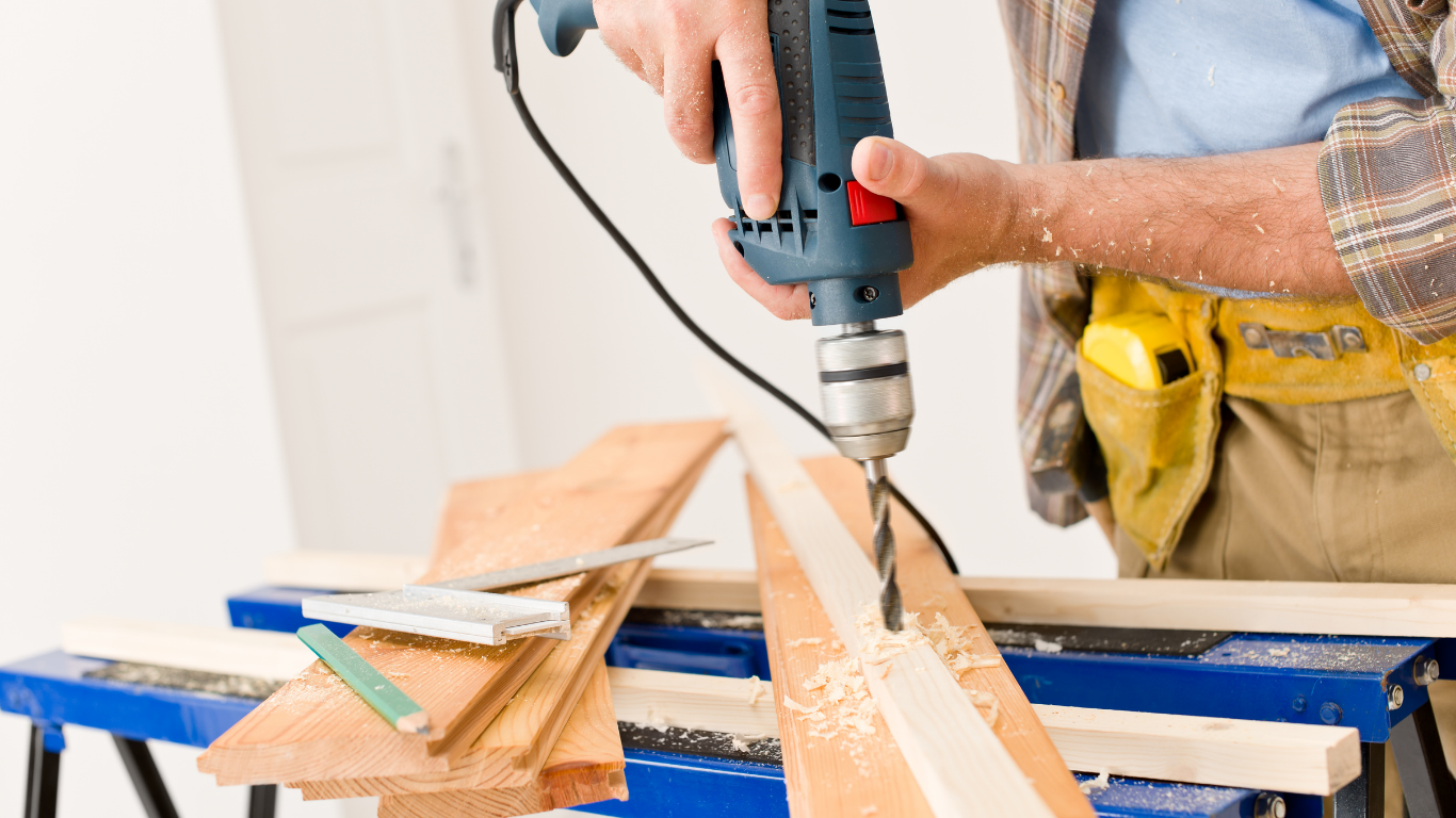 Person using a power drill to bore into a wooden plank on a workbench