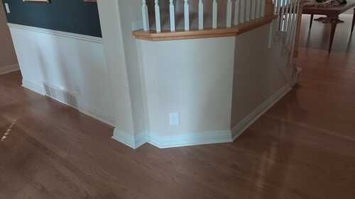 Interior corner with hardwood floors, white railing, and beige walls in a home.