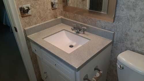 Bathroom vanity with white sink, gray countertop, mirror, and toilet beside it.