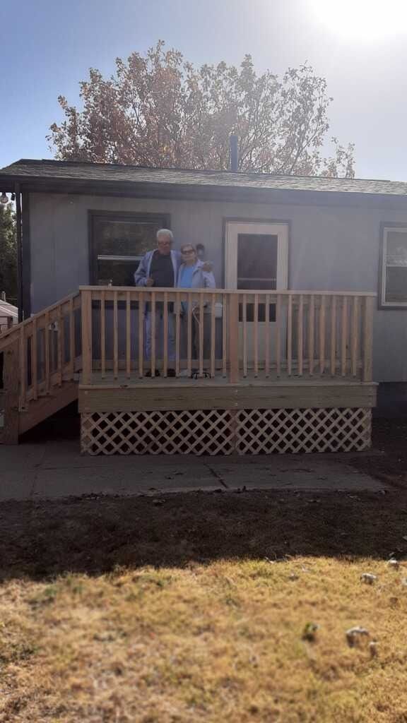 Two people standing on a small front porch of a house in bright sunlight.