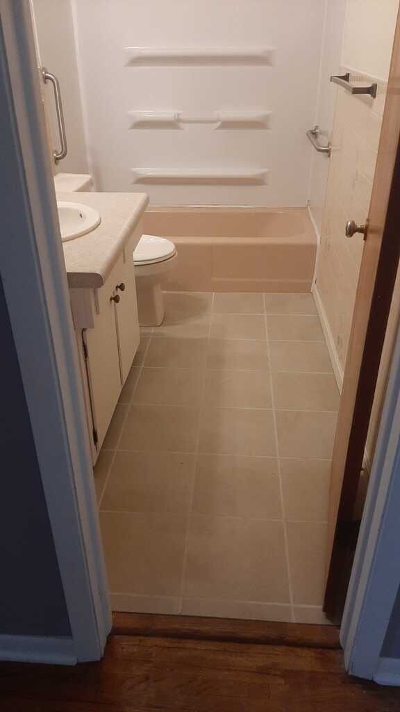 Small bathroom with beige tile floor, white tub, and sink visible through the doorway.