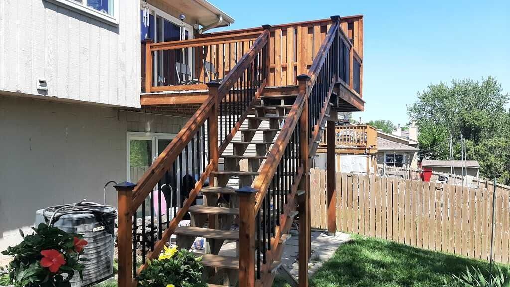 Wooden outdoor stairs with railings leading to a deck beside a house in a backyard
