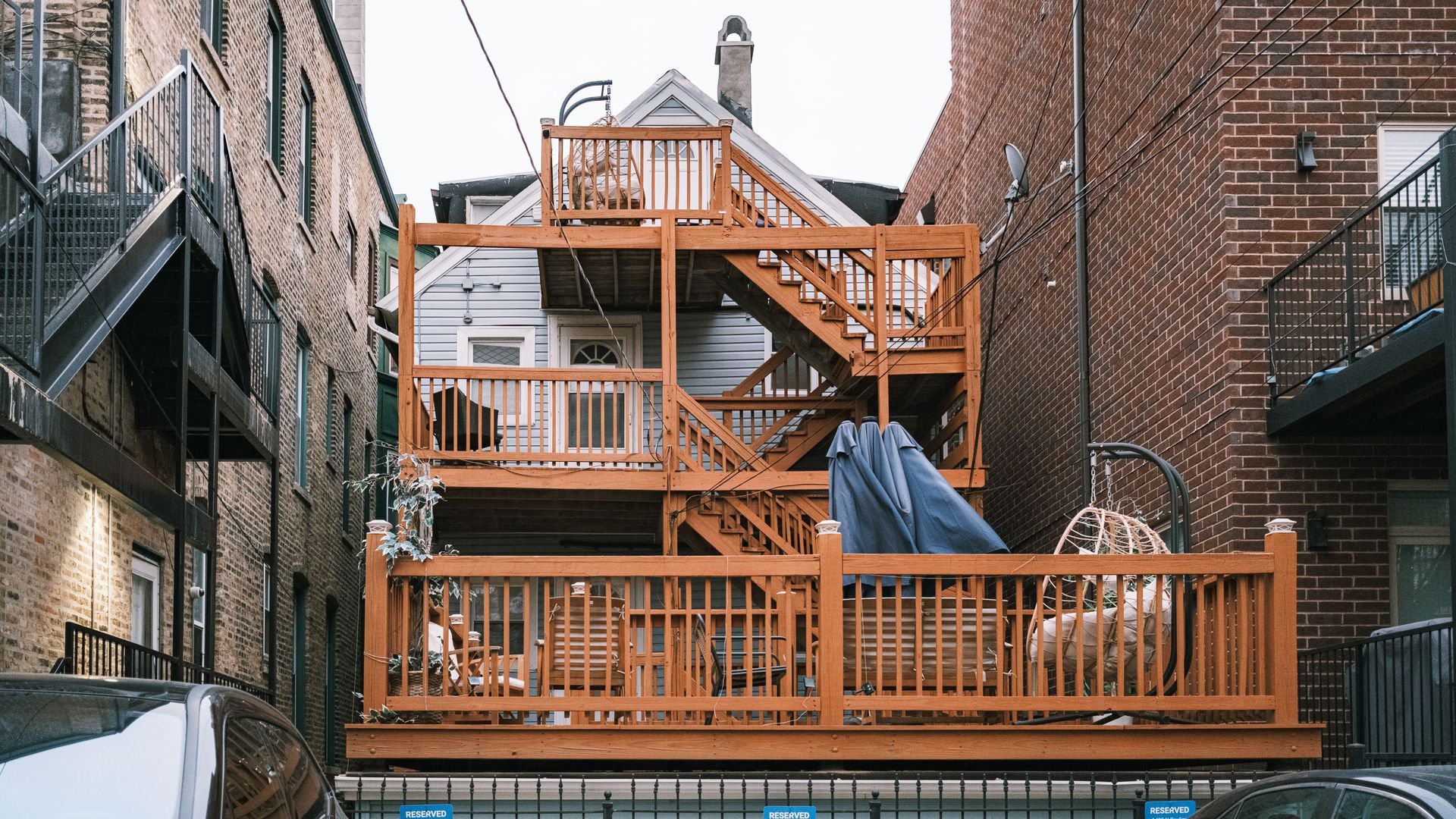 Wooden deck and staircase built between two brick buildings in a narrow urban alley.