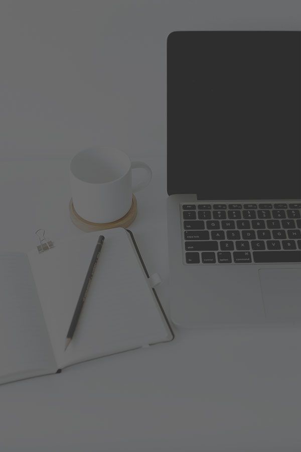 A laptop computer is sitting on a desk next to a cup of coffee and a notebook.