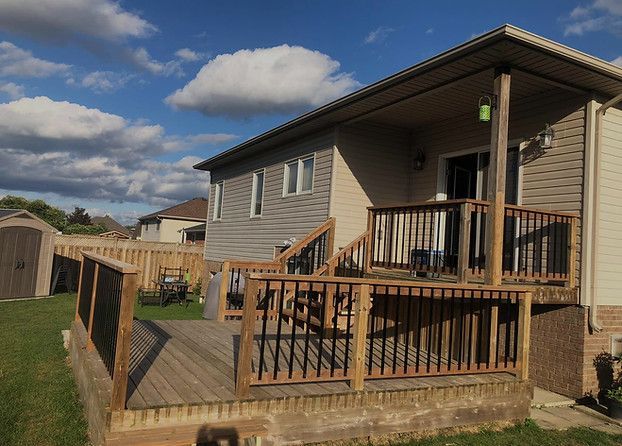 Single-story beige house with a wooden deck and stairs under a blue sky