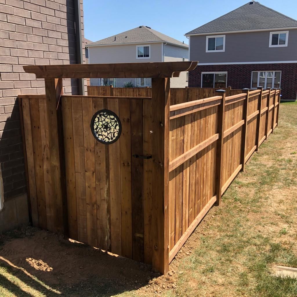 Wooden backyard fence and gate beside a house, with a decorative circular plaque on the gate.