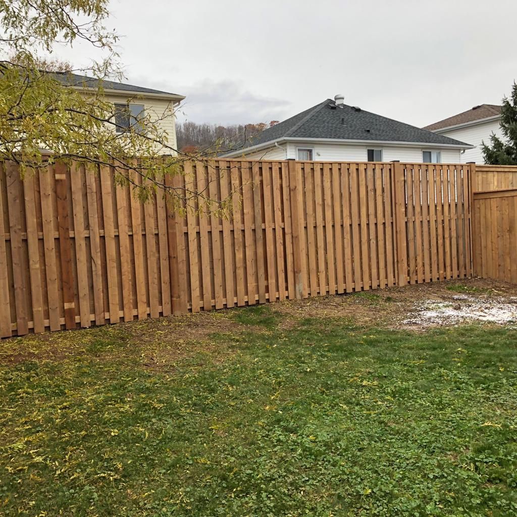 Wooden privacy fence enclosing a grassy backyard with houses visible behind it under a cloudy sky