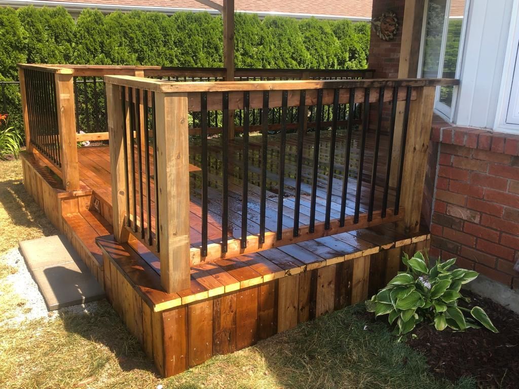 Small wooden accessibility ramp with black railing beside a brick house and steps
