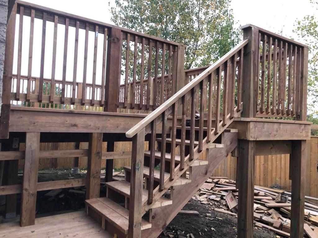 Wooden deck with stairs and railings on a raised outdoor structure, with debris below.