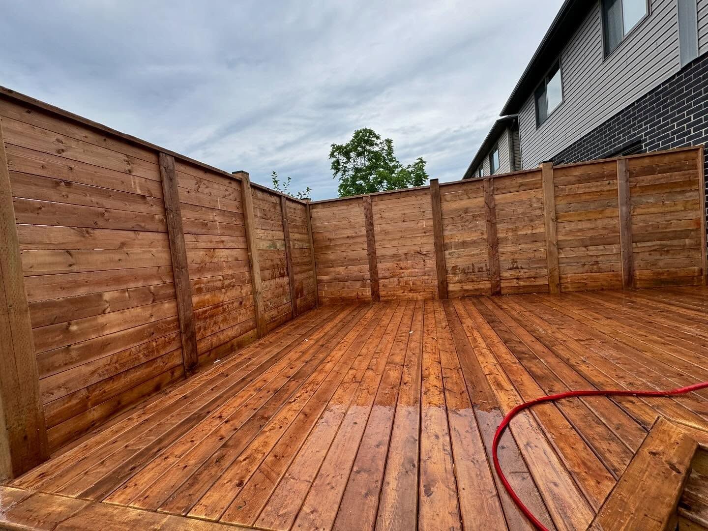 Wooden backyard deck with steps beside a house, bordered by trees and a fenced yard.