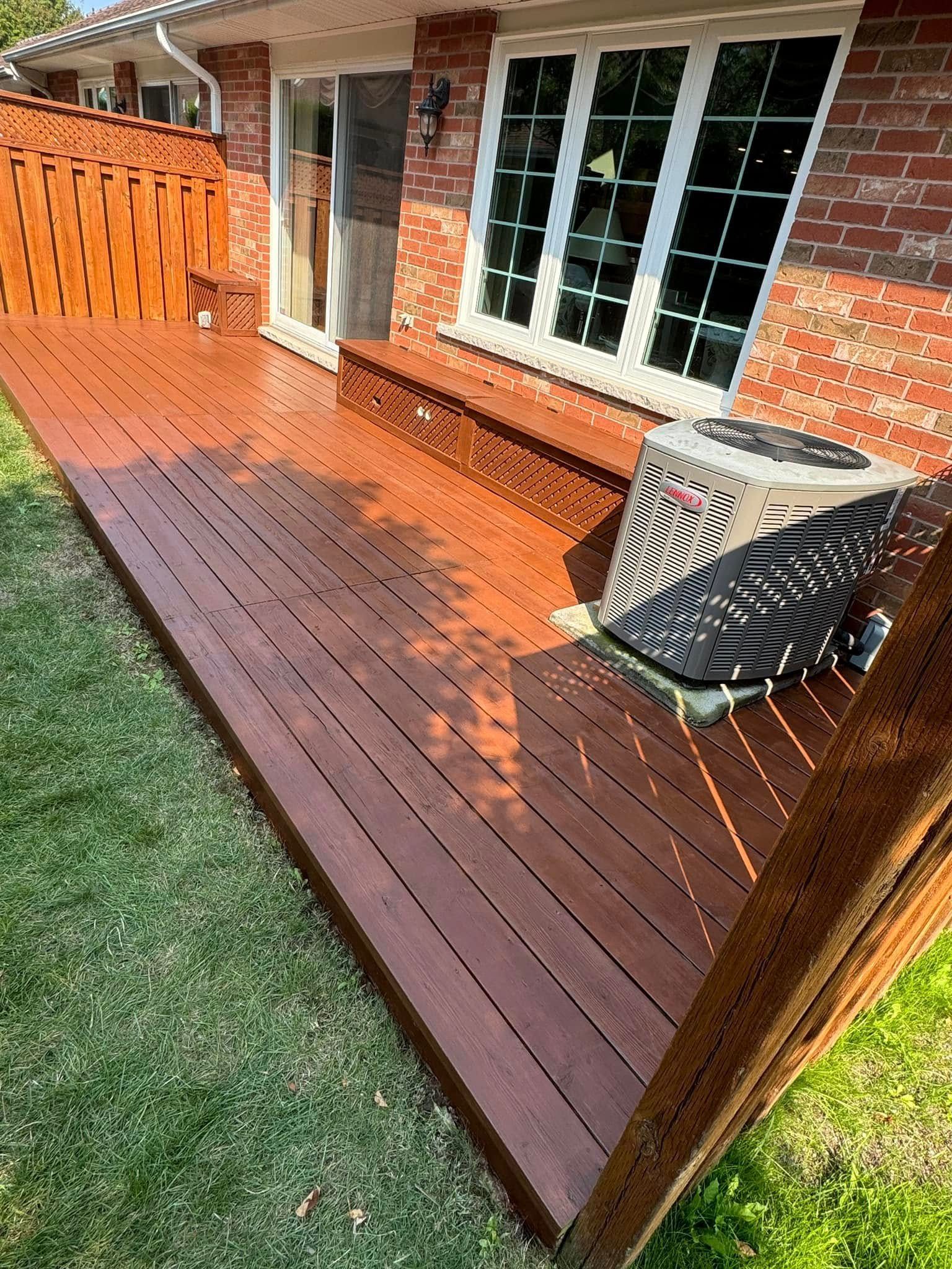 Backyard deck with wooden railing and stairs attached to a gray house, surrounded by green lawn and trees