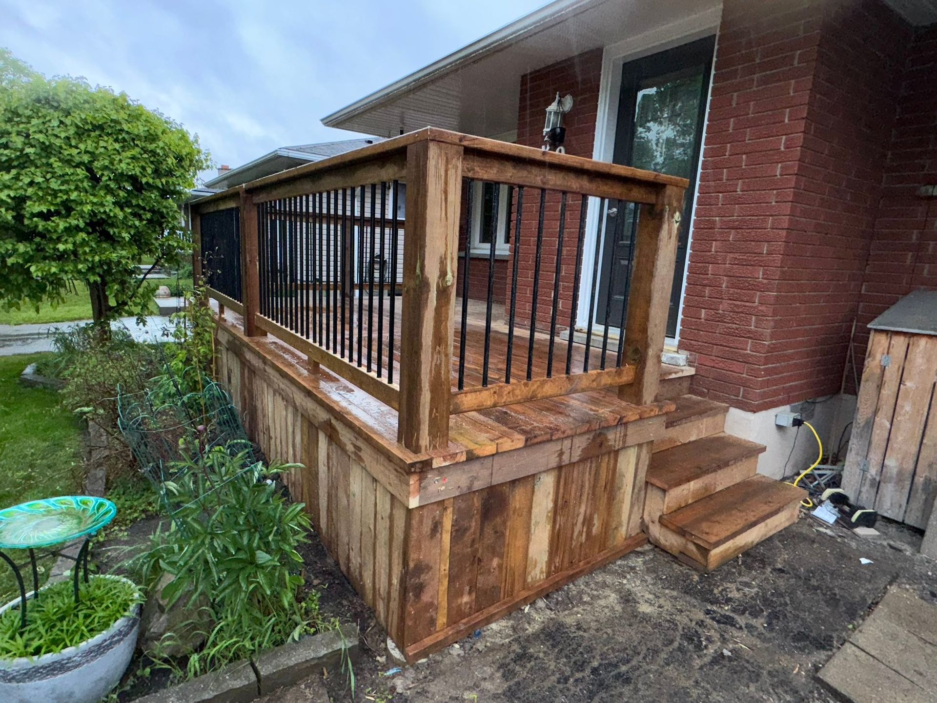 Backyard with red wooden deck, black gazebo, green lawn, and wooden fence under a blue sky