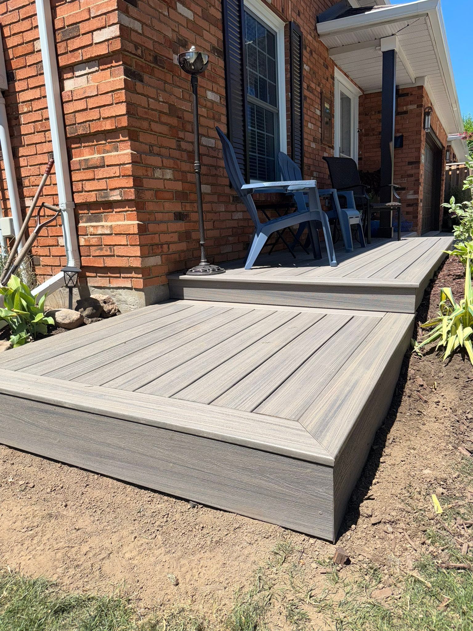 Wooden deck with railing beside a gray house, opening to a wooded backyard under a clear blue sky