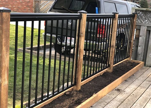 Wooden deck railing with black metal bars beside a driveway and parked black pickup truck