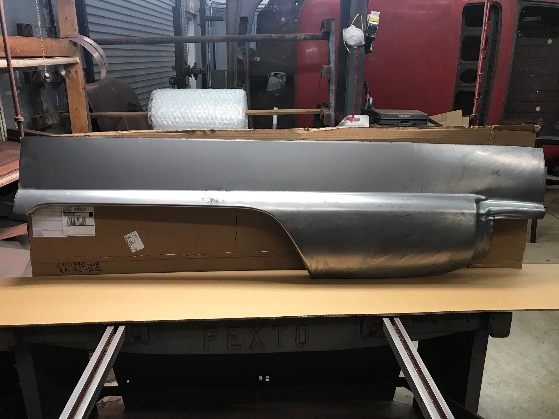 A silver car quarter panel on a cardboard box, in a workshop setting.