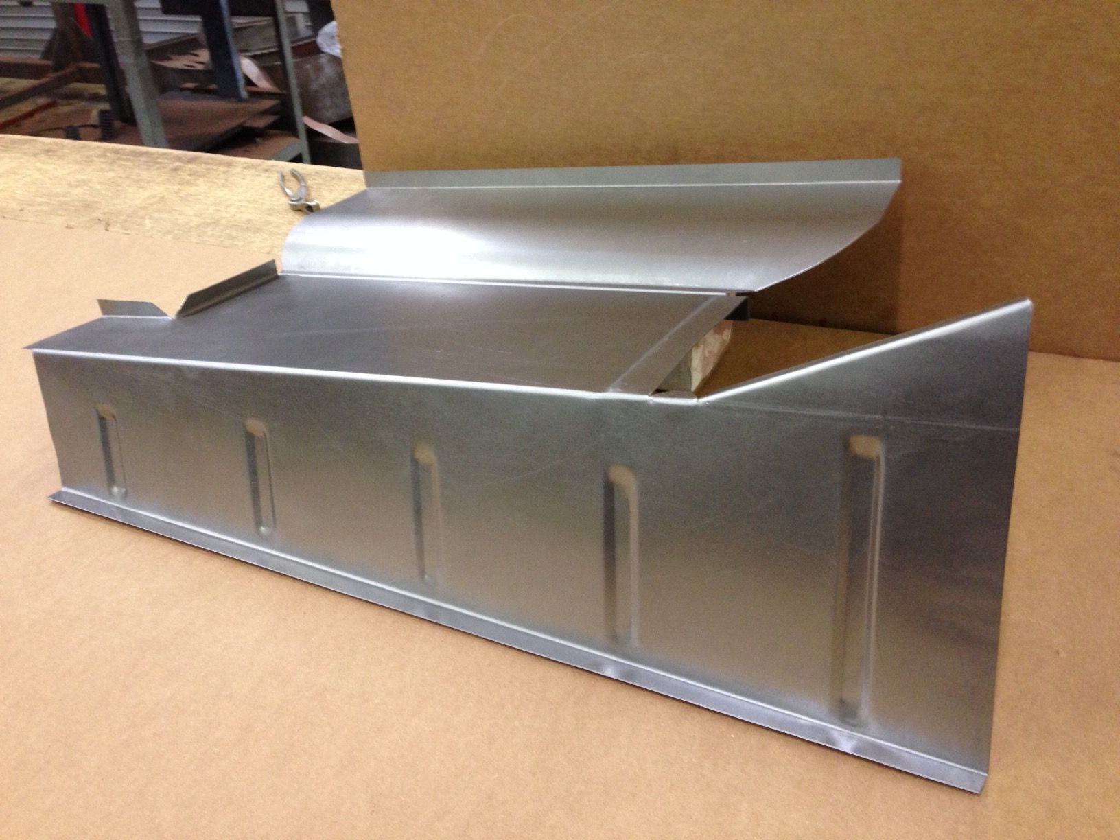 Sheet metal panel on a workbench, silver with a curved edge and folded sides.