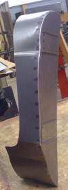 A metal object resembling a curved blade, likely part of a larger machine, resting on a wooden surface.