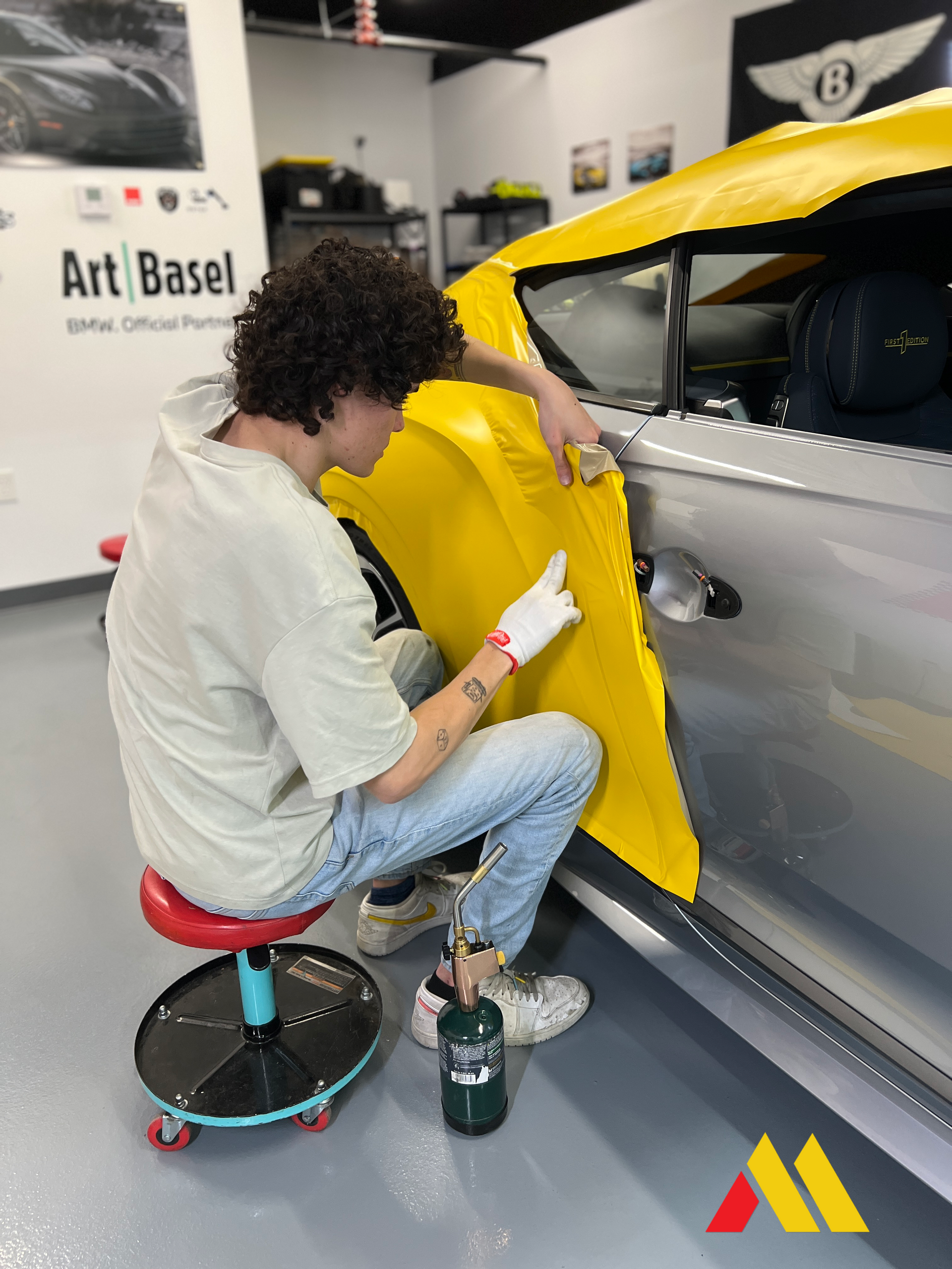 Person wrapping a car in glossy blue vinyl inside a garage