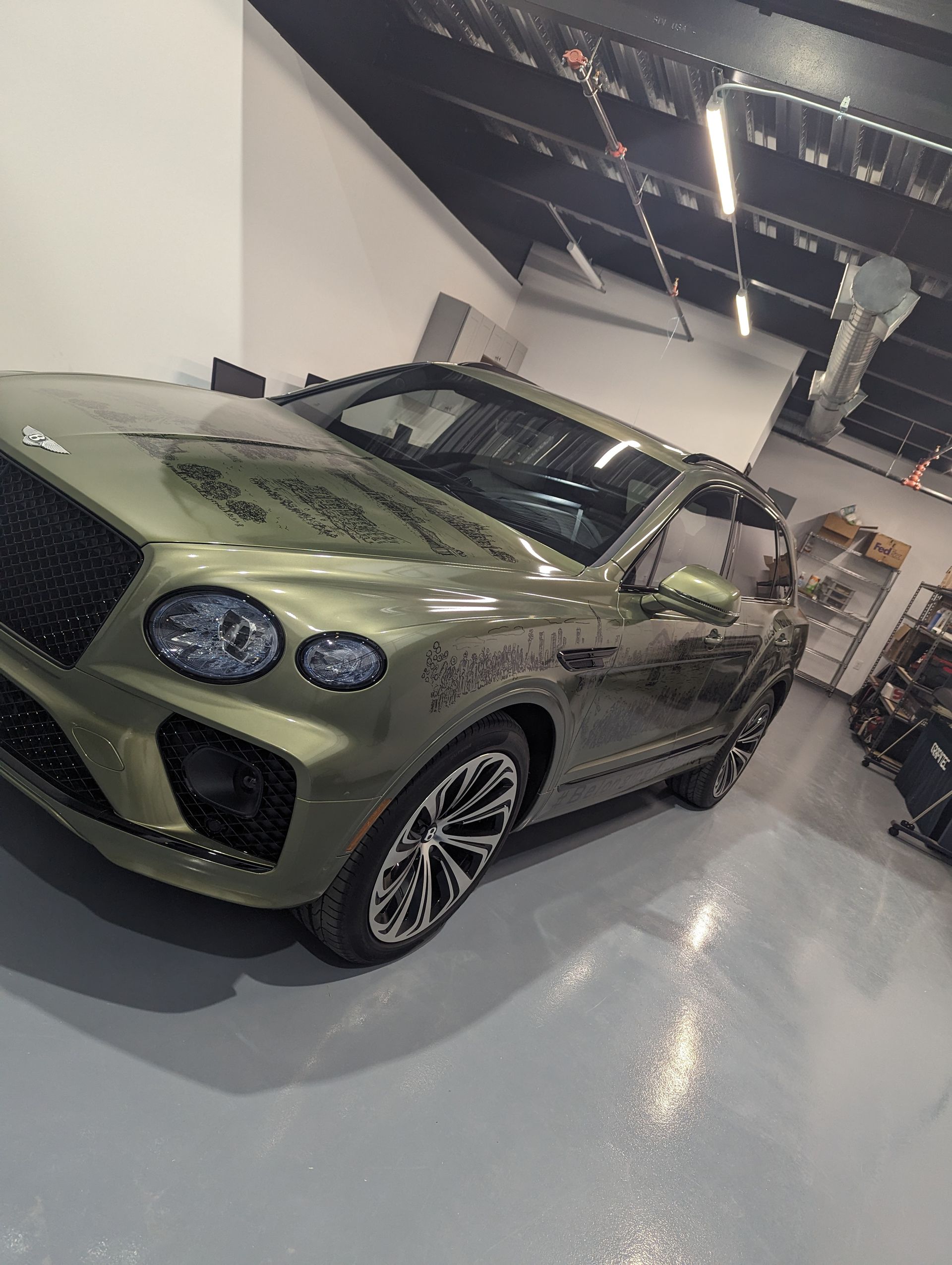 Olive green luxury SUV in a showroom, viewed from the front-left angle.