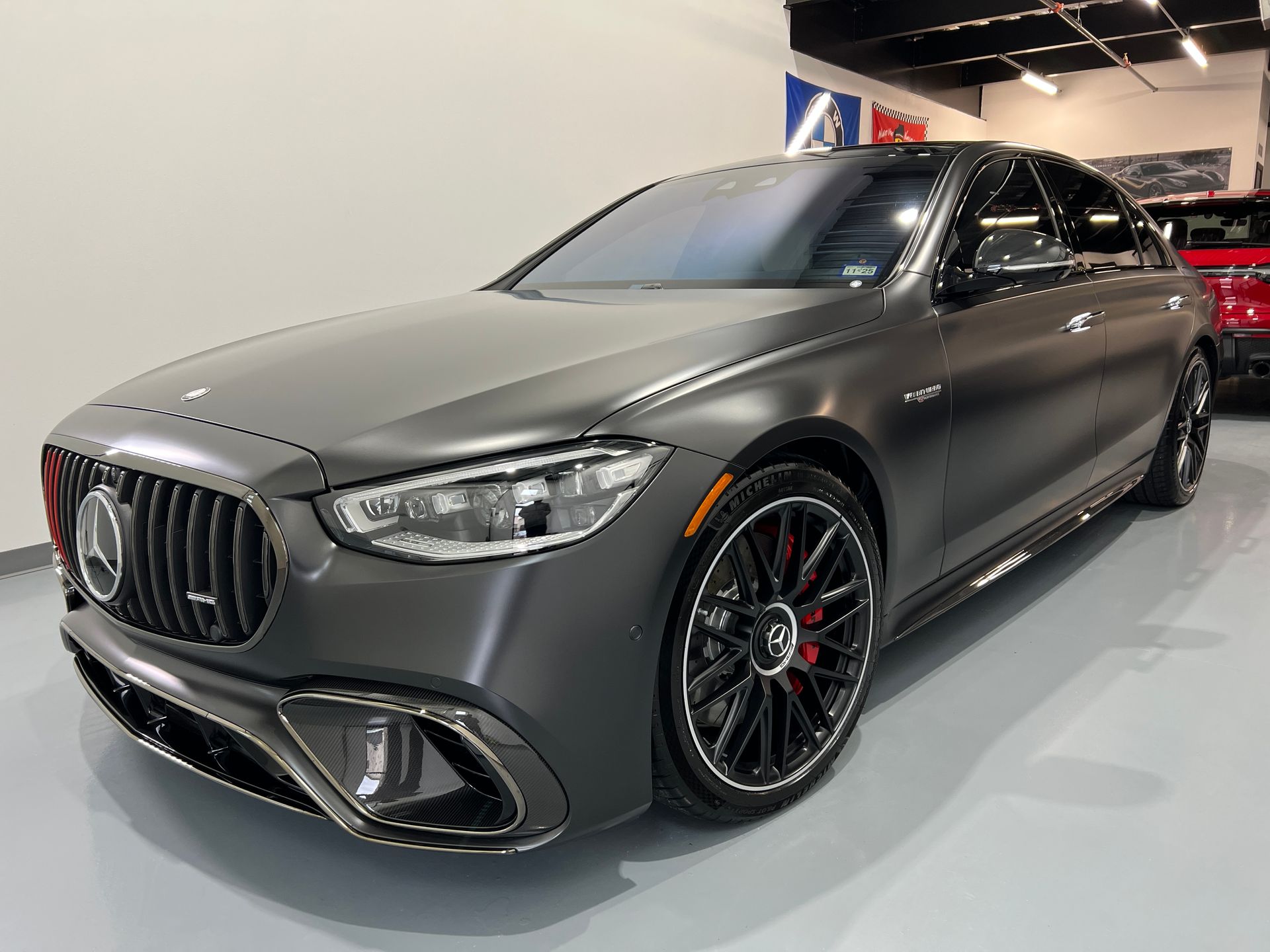 Gray Mercedes-AMG sedan with black wheels and red brake calipers in a showroom.