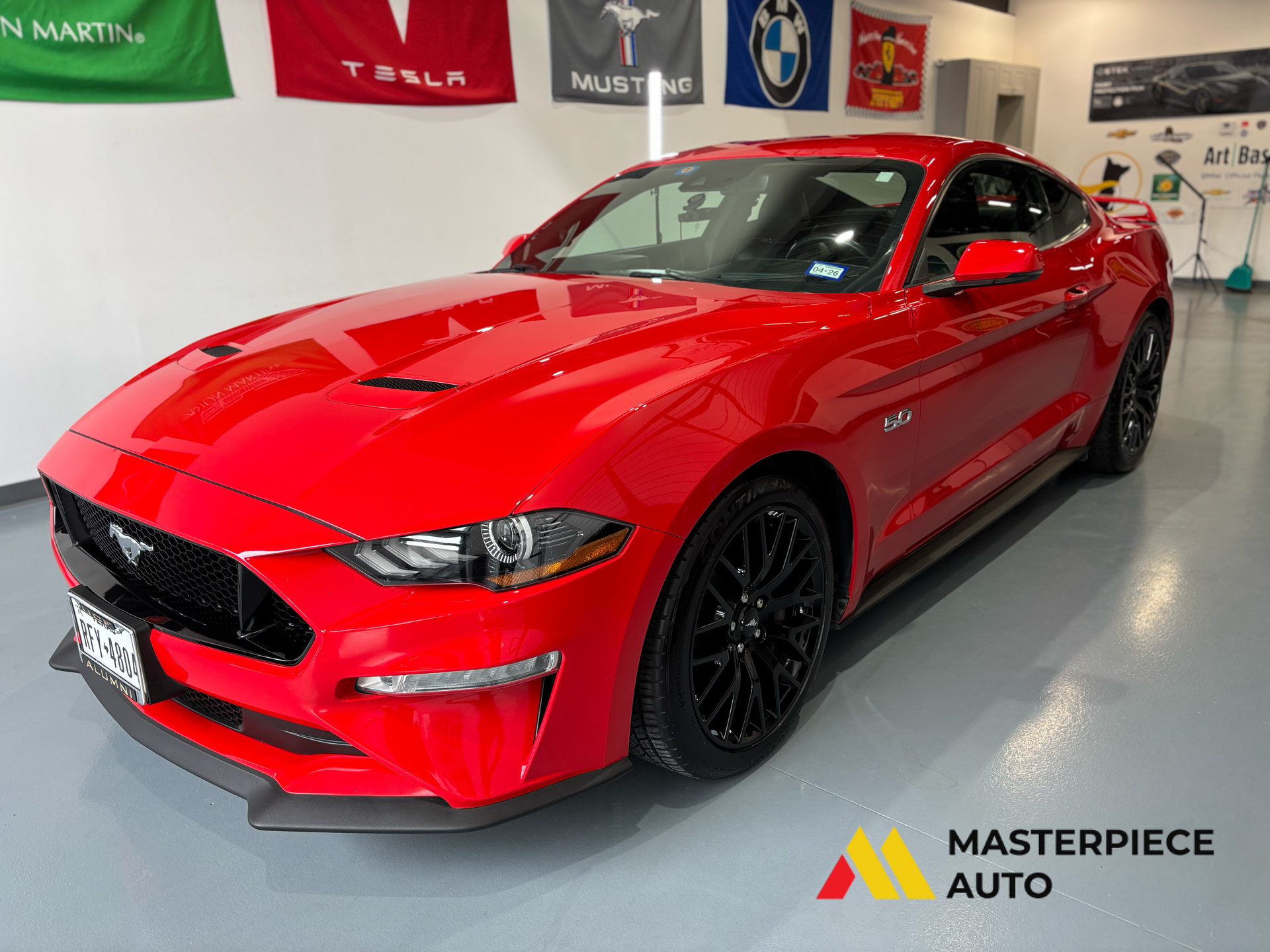 Red sports car in a showroom, front three-quarter view, with red body and black wheels