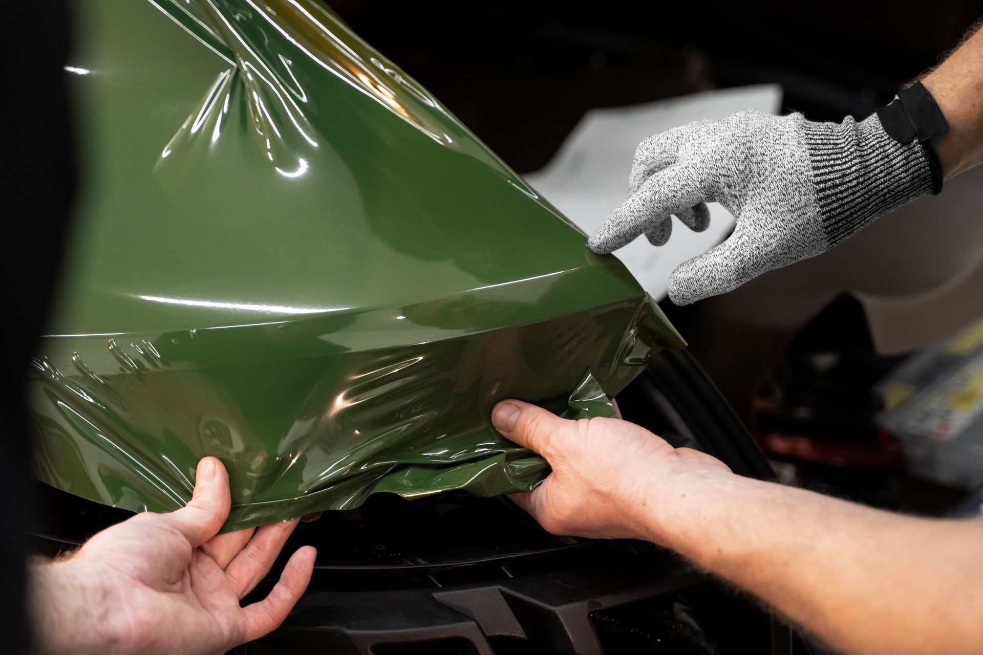 Hands applying yellow car wrap film over a vehicle hood during installation