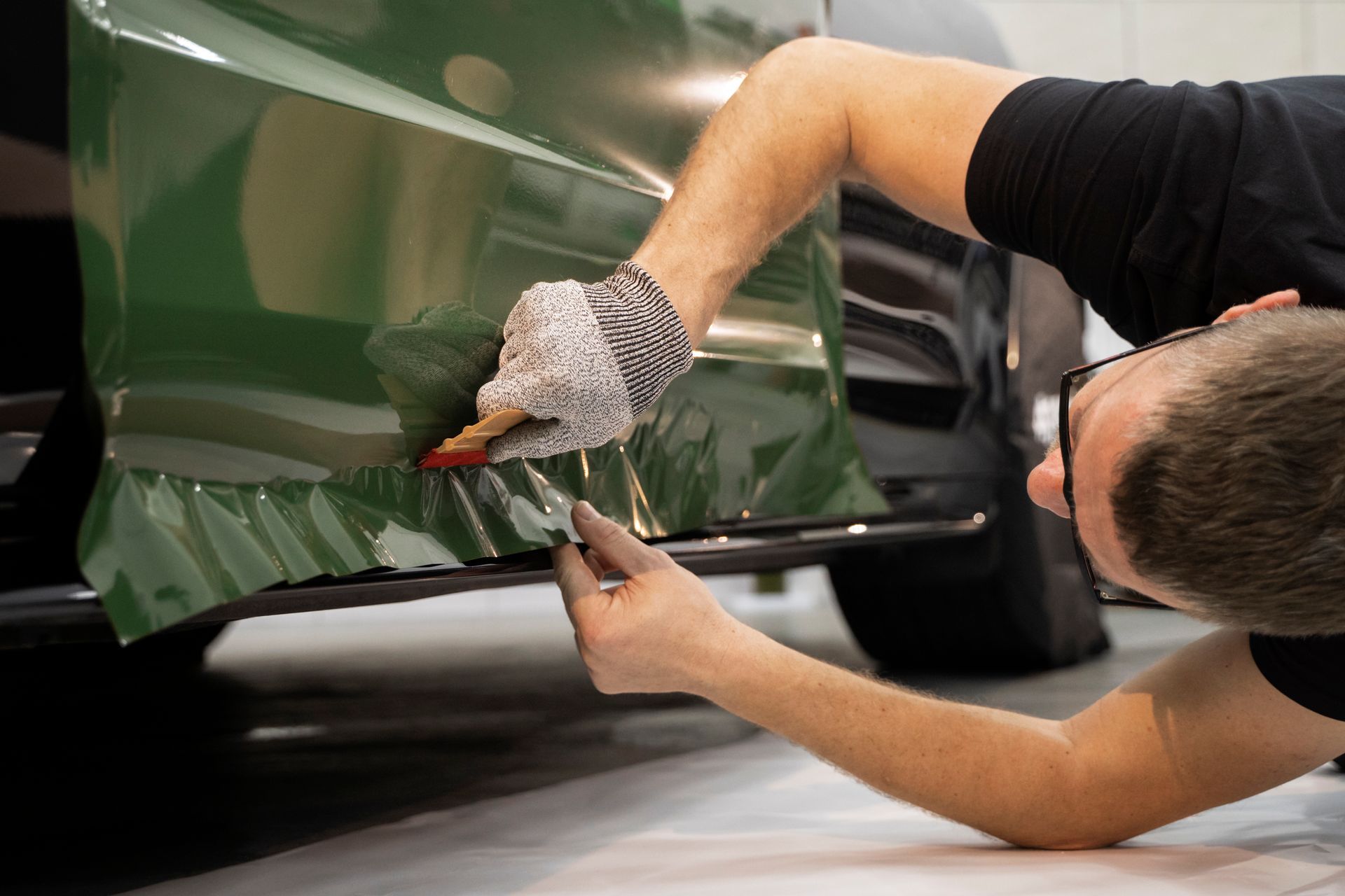 Person applying green vinyl wrap to a car door with a squeegee tool