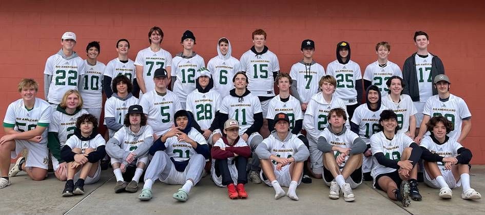 A group of athletes in green and white uniforms posing for a team photo against a red wall.