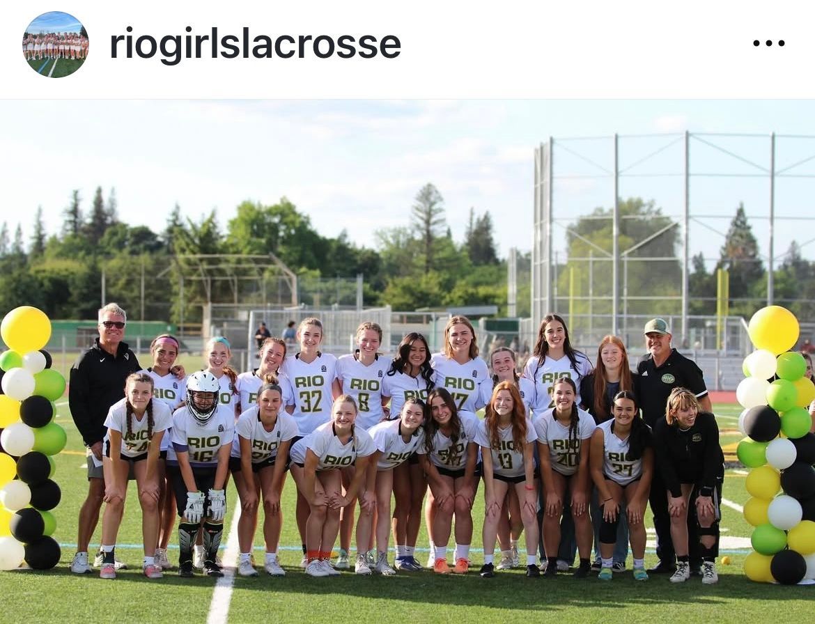 A high school girls lacrosse team posing on a field, flanked by columns of yellow, black, and green balloons.