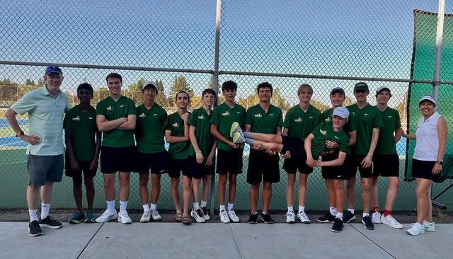 A group of people in matching green uniforms and two coaches standing together on a tennis court.
