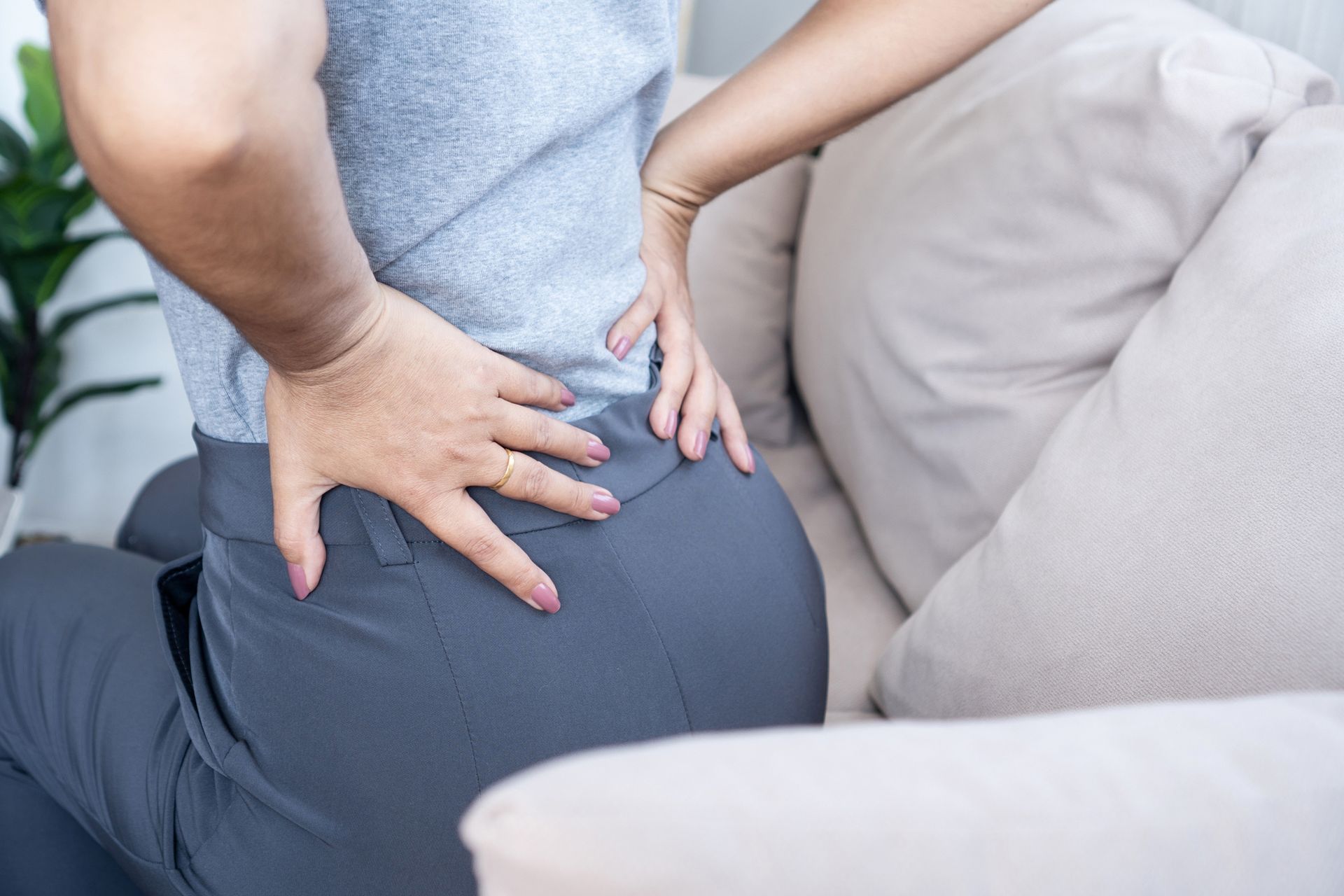 Woman holding her lower back, sitting on a sofa, possibly experiencing pain. Woman holding her lower back, sitting on a sofa, possibly experiencing pain.