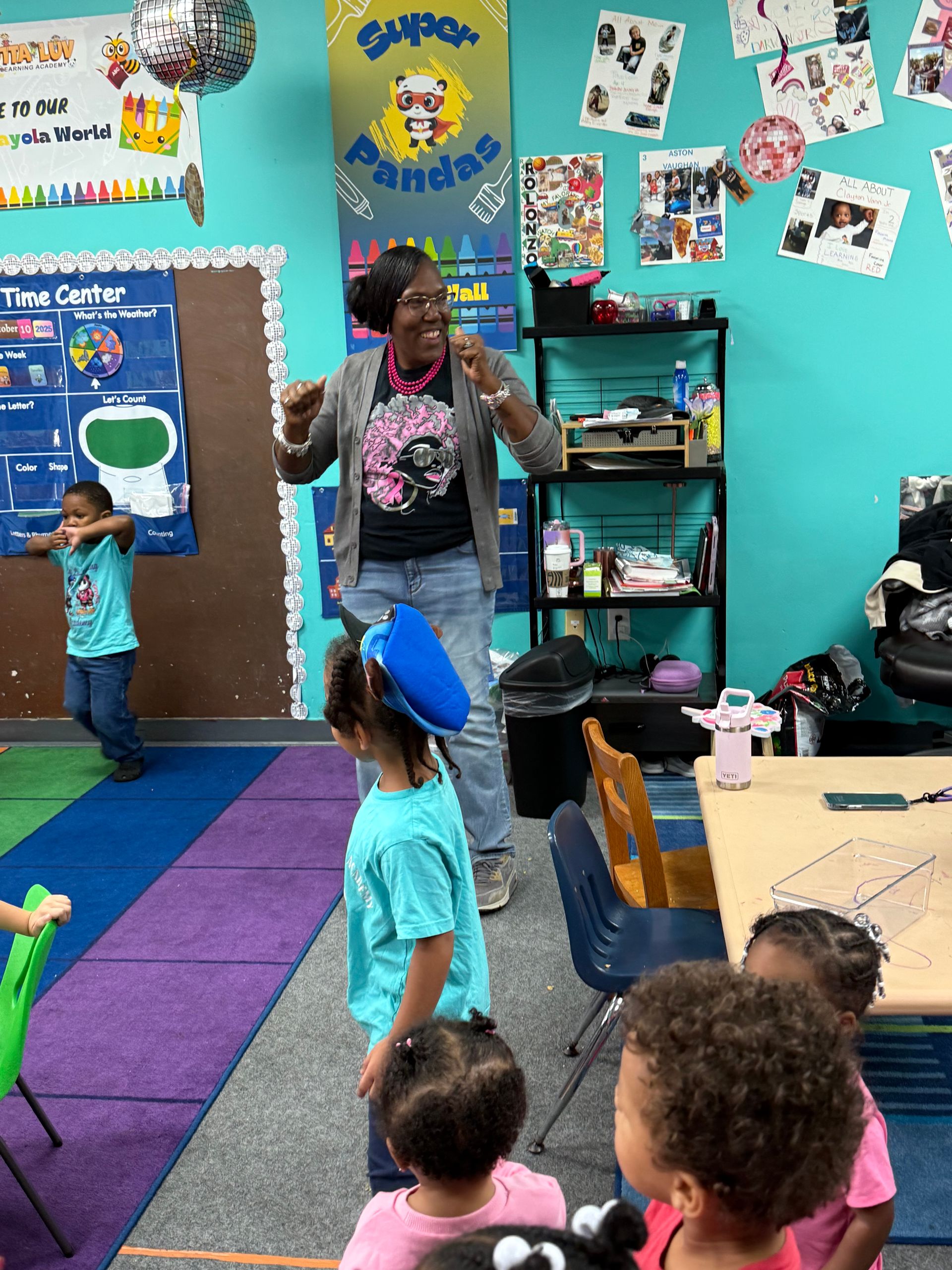Teacher dancing with children in a classroom. Kids are standing and moving; colorful walls.