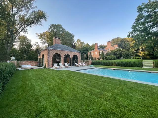 Backyard with manicured lawn, swimming pool, and stone pool house at sunset
