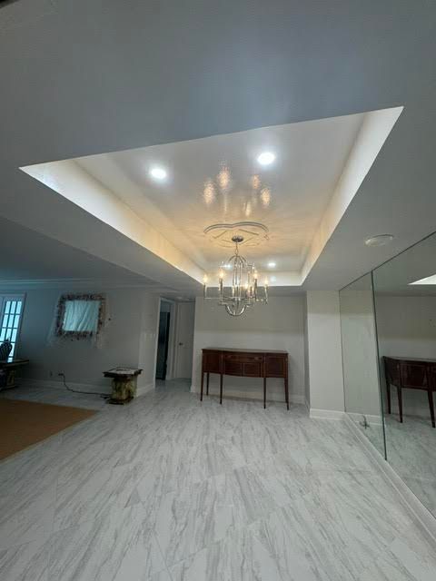 Modern empty living room with recessed ceiling lights, chandelier, mirrored wall, and light wood flooring
