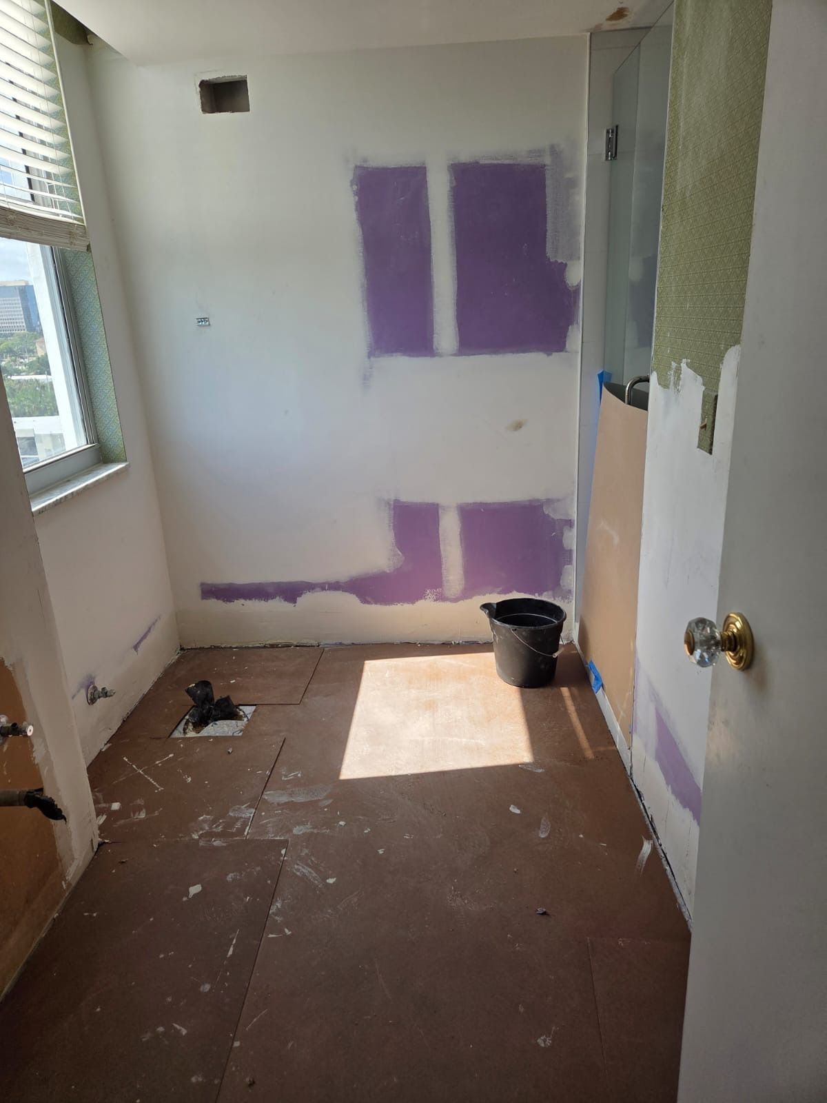 Small room under renovation with purple drywall patches, bare floor, and a bucket by the wall.