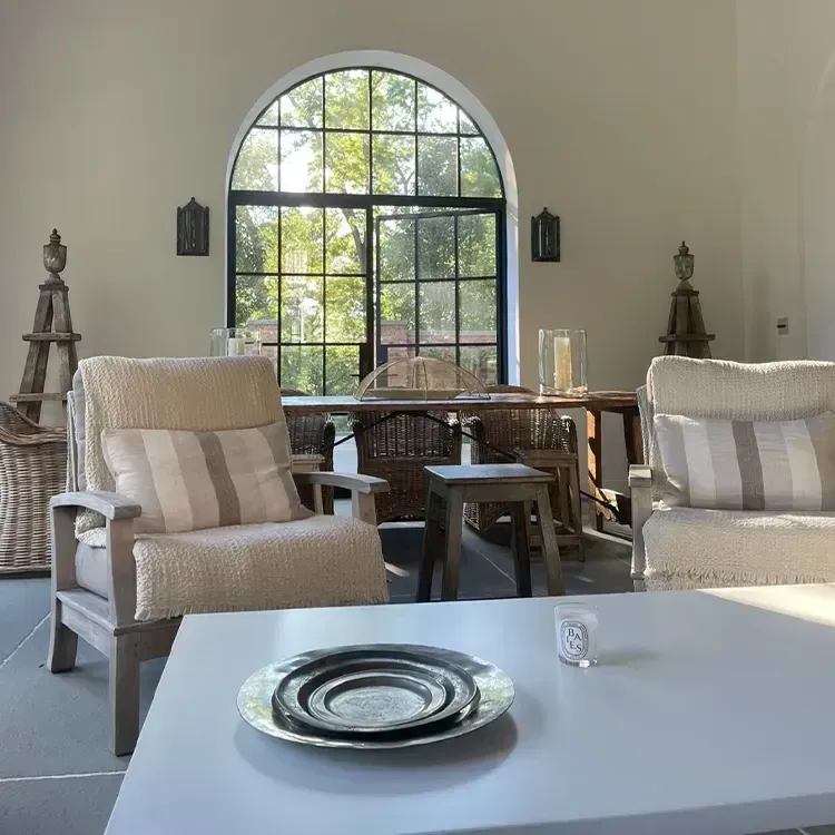 Bright sunroom with arched window, wicker chairs, round table, and white table set with plates