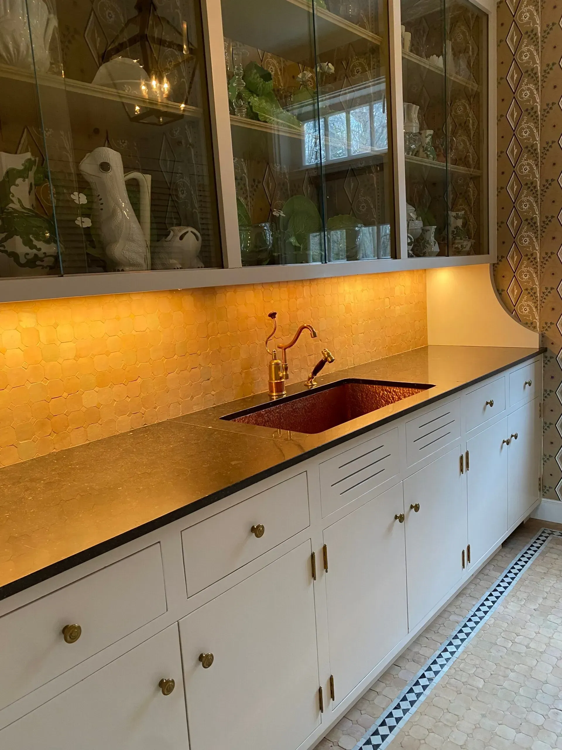 White kitchen counter with sink, cabinets, and glass-front upper cabinets under warm under-cabinet lighting