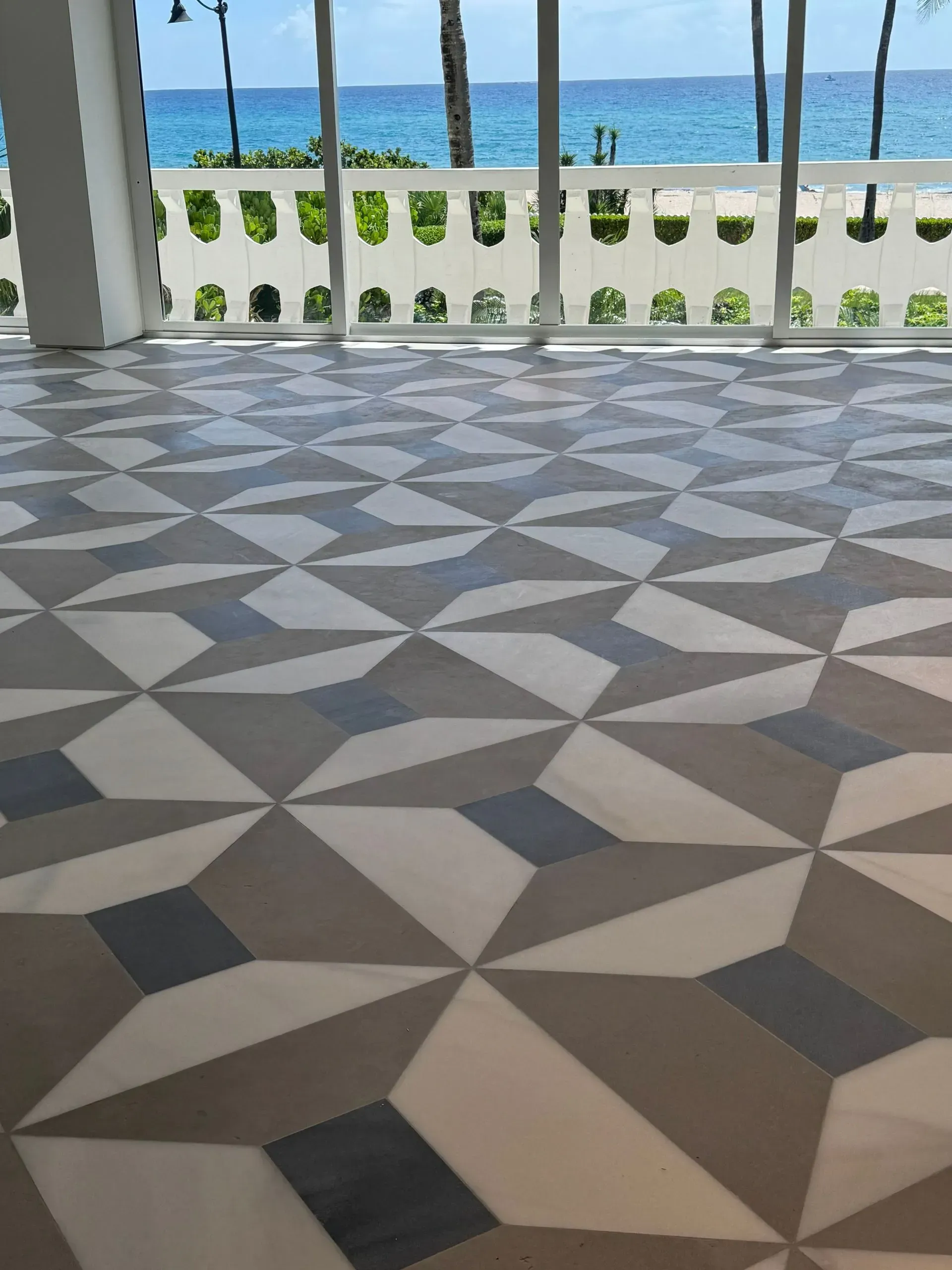 Geometric tiled patio floor overlooking the beach and blue ocean through a white railing