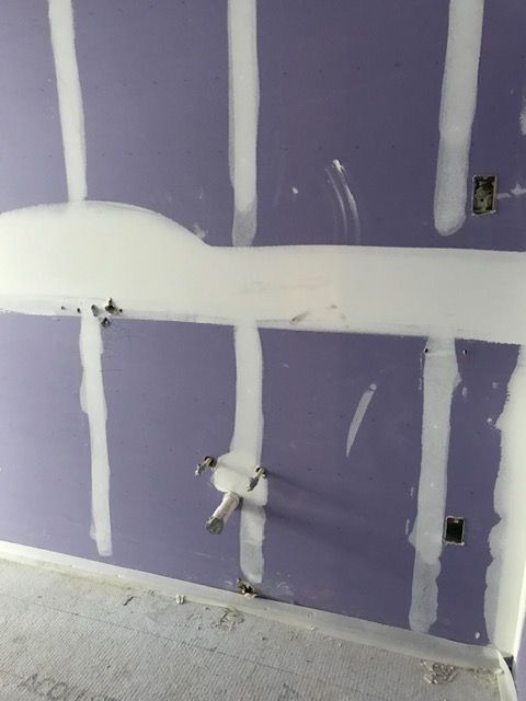 Purple drywall with white joint compound, visible electrical outlets, and a floor outlet opening in an unfinished room