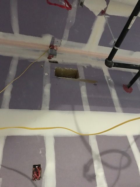 Exposed ceiling with drywall seams, pipes, wiring, and a rectangular cutout during renovation