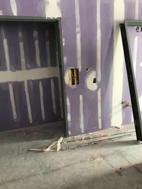 Partially finished purple wall with drywall patches, electrical cutouts, and debris on the floor