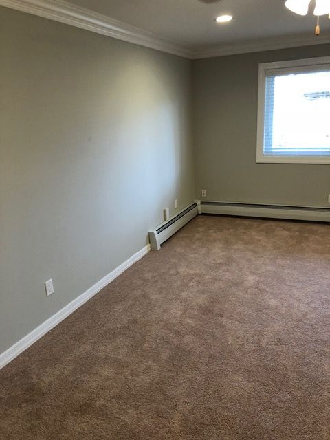 Empty beige bedroom with carpet, white trim, and a window.