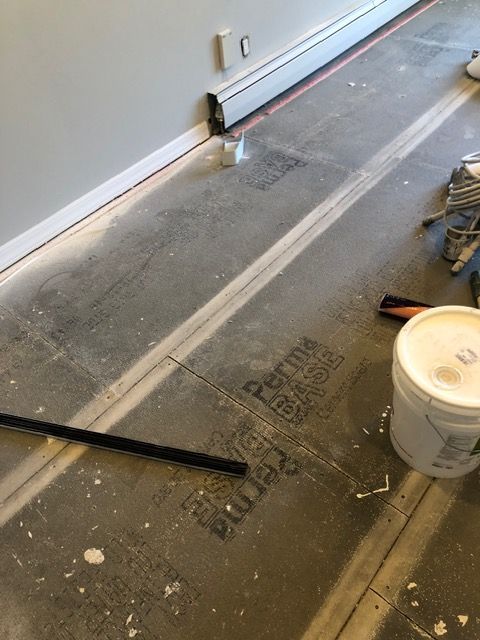 Partially finished room with taped floor, white bucket, and tools near a wall on concrete flooring