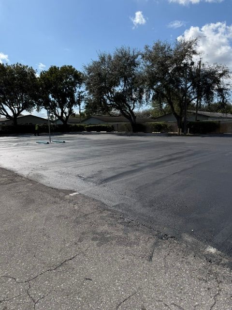 Empty parking lot with cracked asphalt, trees, and a partly cloudy sky