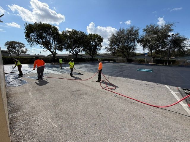 Workers spraying sealant on a parking lot under a bright sky